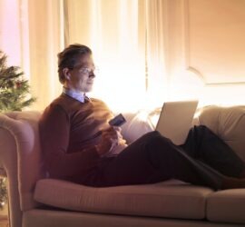 man in brown long sleeve sweater and black pants sitting on brown sofa chair using laptop