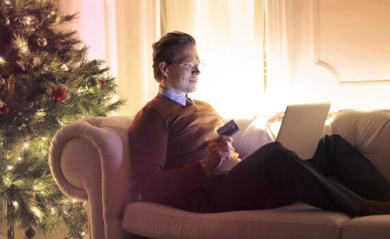 man in brown long sleeve sweater and black pants sitting on brown sofa chair using laptop