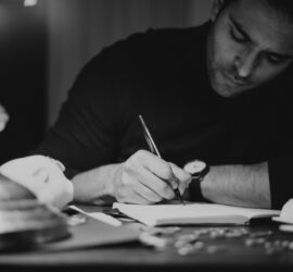 crop man taking notes in copybook in dark home office