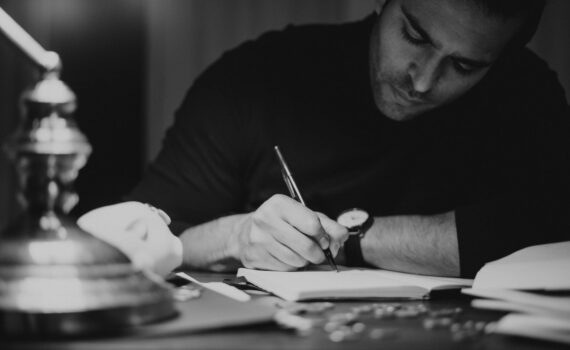 crop man taking notes in copybook in dark home office